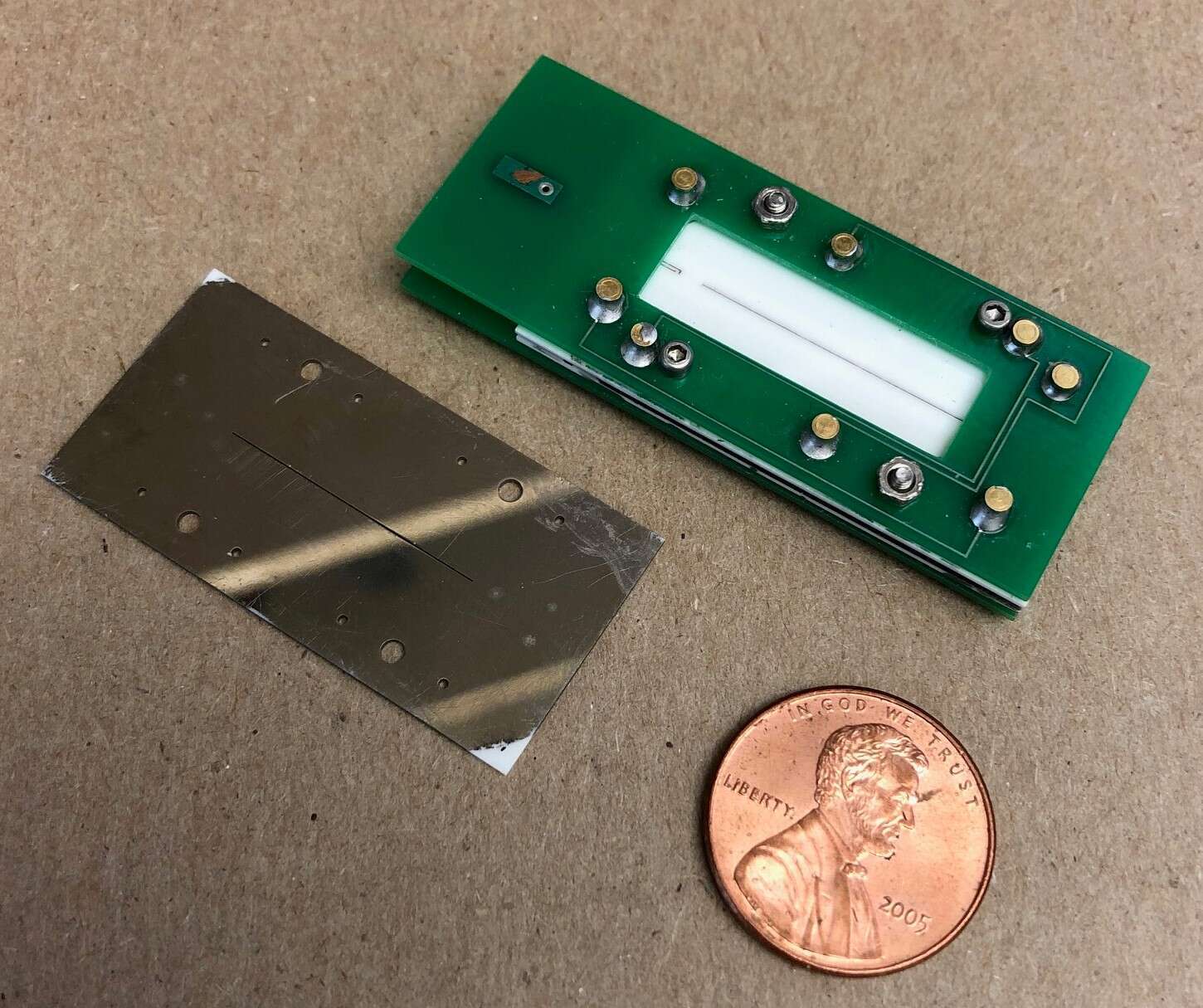 Figure 1: photograph of the ion trap assembly (right, top), a patterned ceramic plate (left), and a U.S. penny.